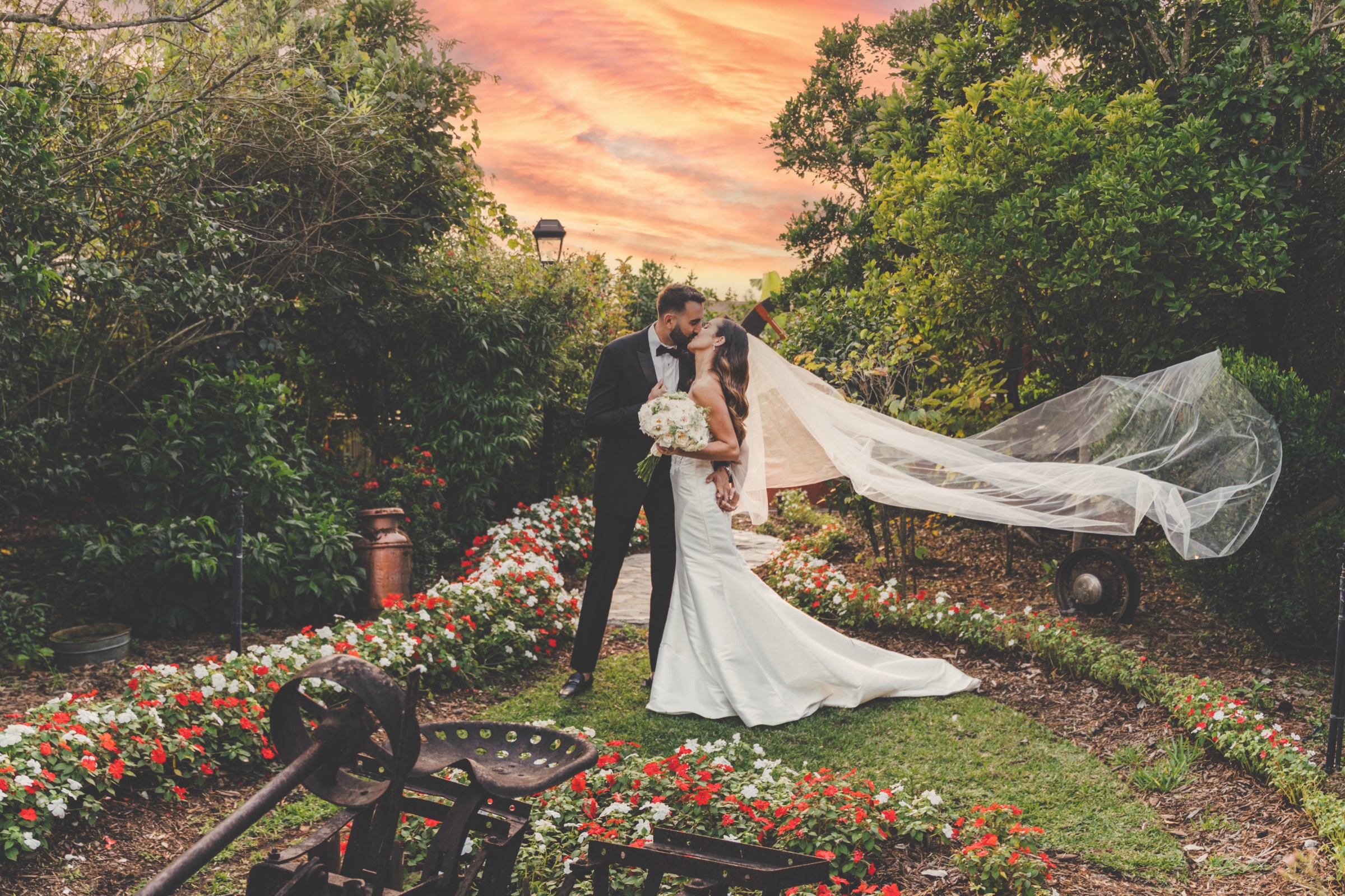 Newlyweds kissing in the estate gardens beneath a sunset sky