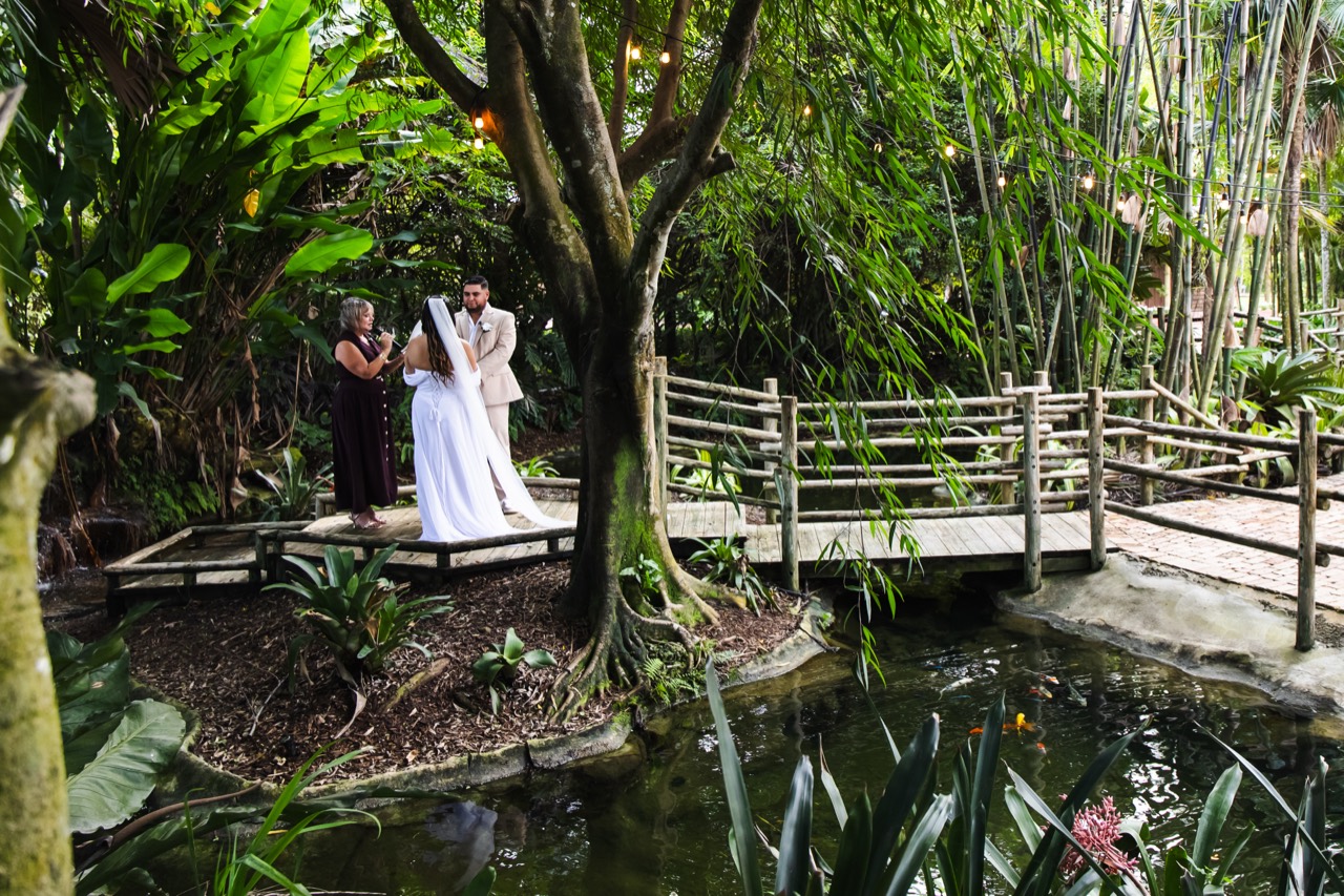 Kaila and Vincent exchanging vows with their officiant on the wooden bridge above the koi pond