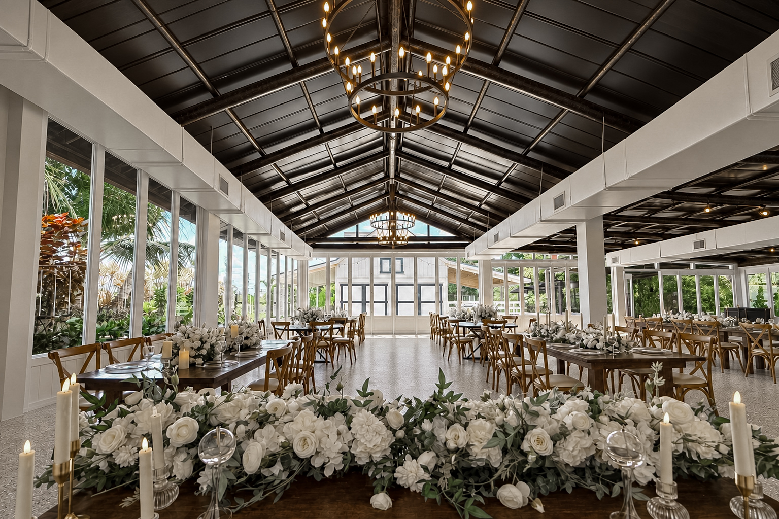 View across a white floral centerpiece toward the chandeliers and glass-lined walls of The Estate Room